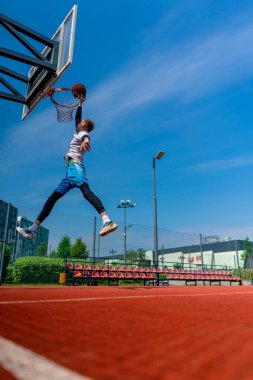 Uzun boylu basketbolcu elinde topla potaya atlıyor. Park 'taki basketbol sahasında yaptığı antrenmanda muhteşem bir smaç yapmak için.