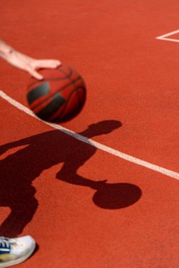 Basketbol sahasının zemininde topa sürerken basketbolcunun gölgesine yakın çekim.