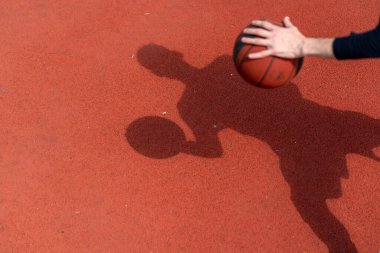 Basketbol sahasının zemininde topa sürerken basketbolcunun gölgesine yakın çekim.