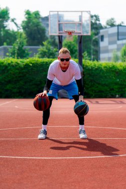 Uzun boylu, iki toplu bir basketbolcu parkta basketbol kortunda çalışırken salya sürme yeteneklerini sergiliyor.