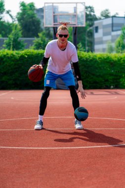 Uzun boylu, iki toplu bir basketbolcu parkta basketbol kortunda çalışırken salya sürme yeteneklerini sergiliyor.