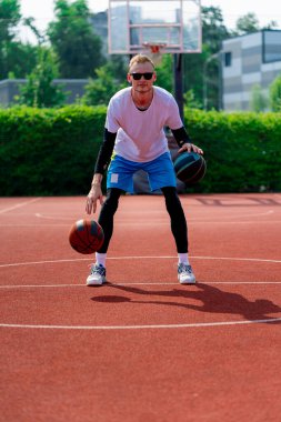 Uzun boylu, iki toplu bir basketbolcu parkta basketbol kortunda çalışırken salya sürme yeteneklerini sergiliyor.