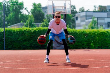 Uzun boylu, iki toplu bir basketbolcu parkta basketbol kortunda çalışırken salya sürme yeteneklerini sergiliyor.