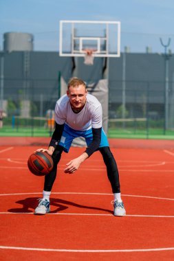 Uzun boylu basketbol oyuncusu parktaki basketbol sahasında top sürme yeteneğini gösteriyor.