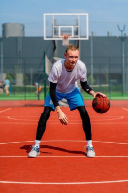 Uzun boylu basketbol oyuncusu parktaki basketbol sahasında top sürme yeteneğini gösteriyor.