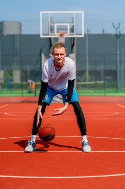 Uzun boylu basketbol oyuncusu parktaki basketbol sahasında top sürme yeteneğini gösteriyor.