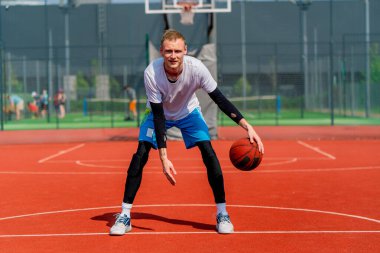 Uzun boylu basketbol oyuncusu parktaki basketbol sahasında top sürme yeteneğini gösteriyor.