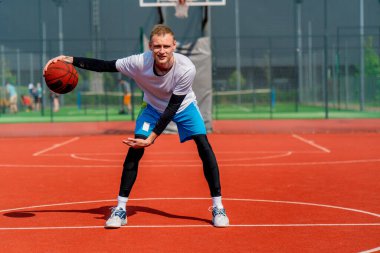 Uzun boylu basketbol oyuncusu parktaki basketbol sahasında top sürme yeteneğini gösteriyor.
