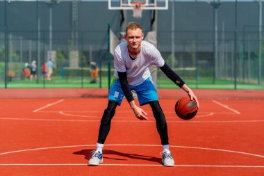 Uzun boylu basketbol oyuncusu parktaki basketbol sahasında top sürme yeteneğini gösteriyor.