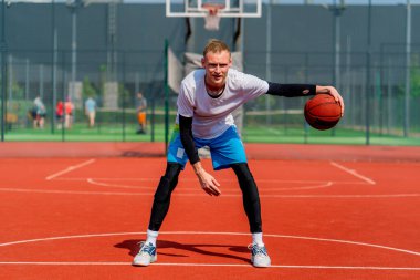 Uzun boylu basketbol oyuncusu parktaki basketbol sahasında top sürme yeteneğini gösteriyor.