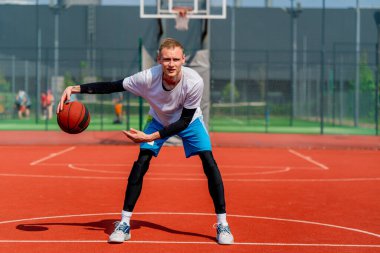 Uzun boylu basketbol oyuncusu parktaki basketbol sahasında top sürme yeteneğini gösteriyor.