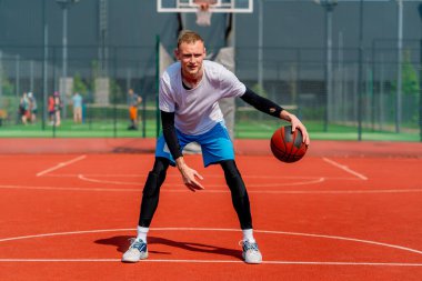 Uzun boylu basketbol oyuncusu parktaki basketbol sahasında top sürme yeteneğini gösteriyor.