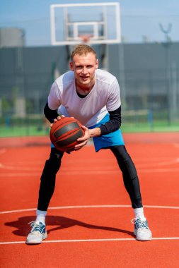 Uzun boylu basketbol oyuncusu parktaki basketbol sahasında top sürme yeteneğini gösteriyor.