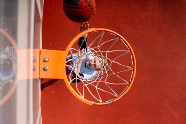 背の高いバスケットボール選手がバスケットボールのゲームを賞賛するというコンセプトの下からボールを投げるバスケットボールリングのクローズアップ — ストック写真