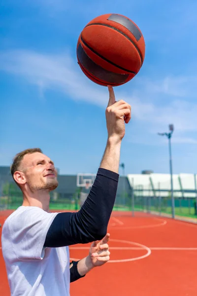 彼のバスケットボールのフリースタイルスキルを示す彼の指にバスケットボールを回転する男のバスケットボール選手のクローズアップ — ストック写真