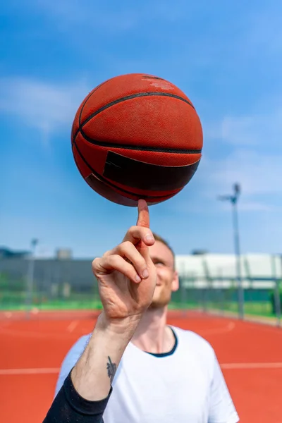 彼のバスケットボールのフリースタイルスキルを示す彼の指にバスケットボールを回転する男のバスケットボール選手のクローズアップ — ストック写真