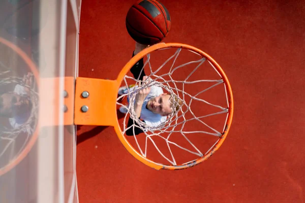 背の高いバスケットボール選手がバスケットボールのゲームを賞賛するというコンセプトの下からボールを投げるバスケットボールリングのクローズアップ — ストック写真