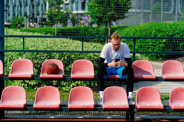 Alto Jogador Basquete Cara Senta Olhando Para Smartphone Nas Bancadas — Fotografia de Stock