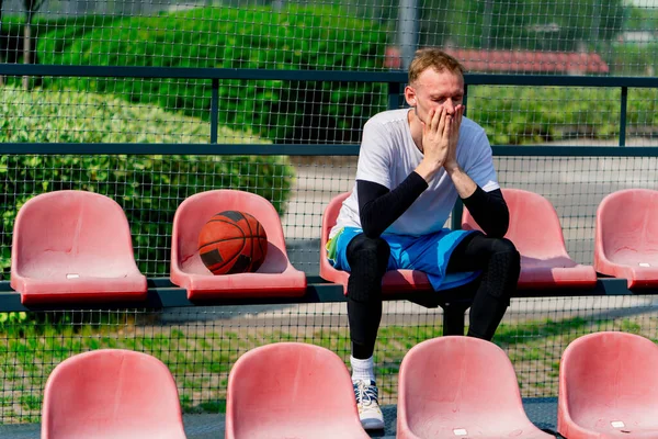 Vysoký Frustrovaný Chlap Basketbalista Sedí Tribunách Basketbalového Hřiště Míčem Boku — Stock fotografie