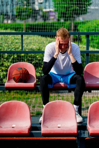 Высокий Разочарованный Парень Баскетболист Сидящий Трибунах Баскетбольной Площадки Мячом Рядом — стоковое фото