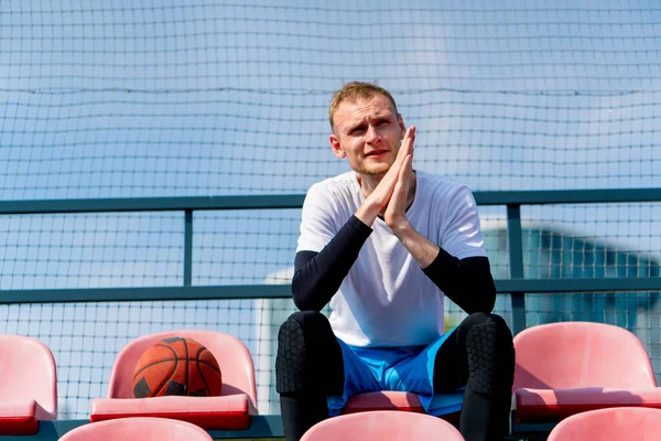 Basketbol sahasının tribünlerinde oturan uzun ve sinirli basketbol oyuncusu.