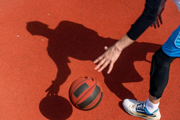 Basketbol sahasının zemininde topa sürerken basketbolcunun gölgesine yakın çekim.