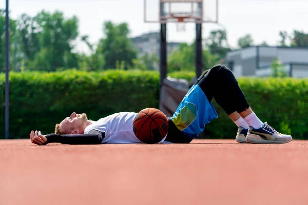 Tall guy basketball player lying on a basketball court in the park along with  basketball resting during practice