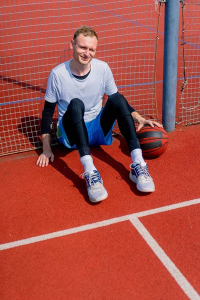 Высокий Баскетболист Мячом Руке Сидит Опираясь Сетку Баскетбольной Площадки Время — стоковое фото