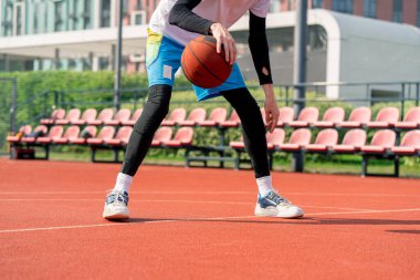 Uzun boylu basketbol oyuncusu parktaki basketbol sahasında top sürme yeteneğini gösteriyor.