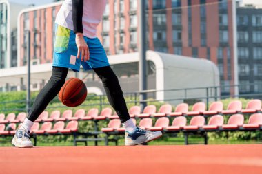 Uzun boylu basketbol oyuncusu parktaki basketbol sahasında top sürme yeteneğini gösteriyor.