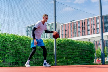 Uzun boylu basketbol oyuncusu parktaki basketbol sahasında top sürme yeteneğini gösteriyor.