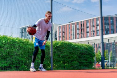 Uzun boylu basketbol oyuncusu parktaki basketbol sahasında top sürme yeteneğini gösteriyor.