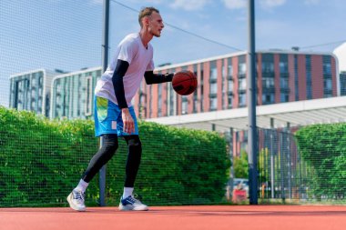 Uzun boylu basketbol oyuncusu parktaki basketbol sahasında top sürme yeteneğini gösteriyor.