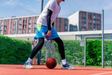 Uzun boylu basketbol oyuncusu parktaki basketbol sahasında top sürme yeteneğini gösteriyor.