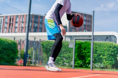 Uzun boylu basketbol oyuncusu parktaki basketbol sahasında top sürme yeteneğini gösteriyor.