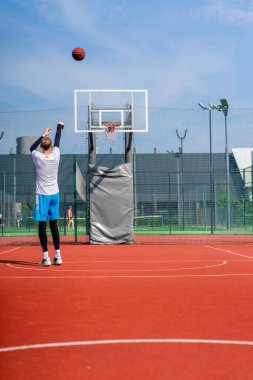 Uzun boylu basketbolcu antrenman sırasında parkta basketbol sahasında basket potasına top atıyor.