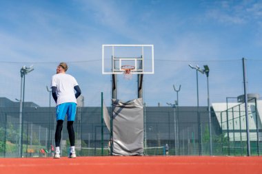 Uzun boylu basketbolcu antrenman sırasında parkta basketbol sahasında basket potasına top atıyor.
