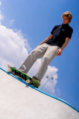 Genç bir kaykaycı şehir kaykay parkında gökyüzü ve bulutlara karşı bir kaykay havuzunun kenarında duruyor.