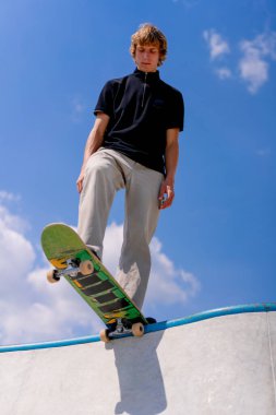 Genç bir kaykaycı şehir kaykay parkında gökyüzü ve bulutlara karşı bir kaykay havuzunun kenarında duruyor.