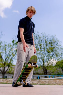 Genç bir kaykaycı kaykay yapmaya başlamadan önce elinde kaykayla parkta duruyor.