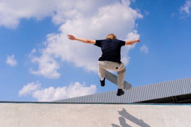 Genç bir kaykaycı şehir kaykay parkında gökyüzü ve bulutlara karşı bir buz pateni pistinin kenarında gösteri yapıyor.