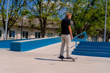 Şehirdeki kaykay pistinde uzun saçlı genç kaykaycı telefonda konuşuyor.