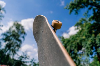 Kaykaycının elinde tuttuğu kaykayın yakın çekimi arka plandaki gökyüzüne karşı.