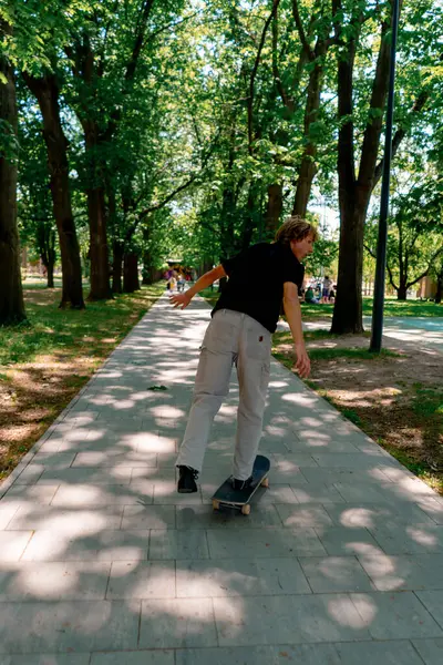 小伙子在公园的小路上 靠着树木和天空滑板滑行 — 图库照片