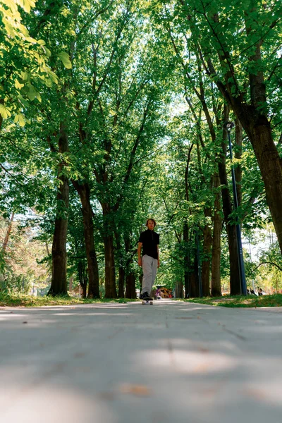 小伙子在公园的小路上 靠着树木和天空滑板滑行 — 图库照片