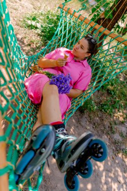 Parktaki bir hamakta uzanmış paten kaymaktan ve dondurma yemekten dinlenen genç kız.