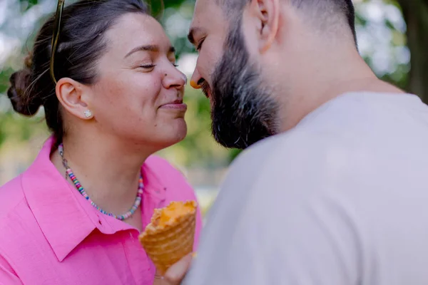 若いカップル男は公園で日付の間に彼女の手にアイスクリームを保持している女の子にキス — ストック写真
