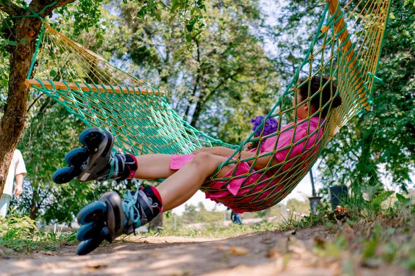 stock image A girl in a pink dress wearing roller skates with a bouquet of flowers in her hands is lying on hammock in the park