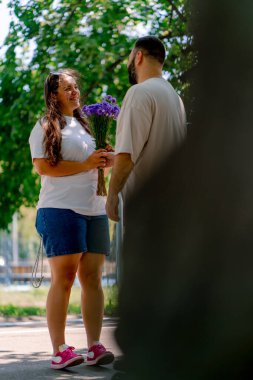 Randevu sırasında parkta kıza çiçek veren neşeli genç bir çift. Ağaçların arka planına ve boyut modellerine karşı.