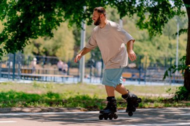 Sakallı genç adam şehir parkında paten kaymayı öğreniyor. Yeni şeyler öğrenmek ve vücut pozitifliği.